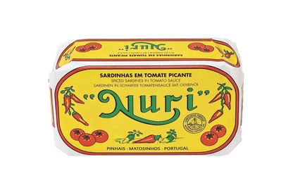 A tin of Nuri Spiced Sardines in Tomato Sauce, featuring a bright yellow label with green 'Nuri' lettering and illustrations of red tomatoes and chili peppers, shown on a transparent checkerboard background.